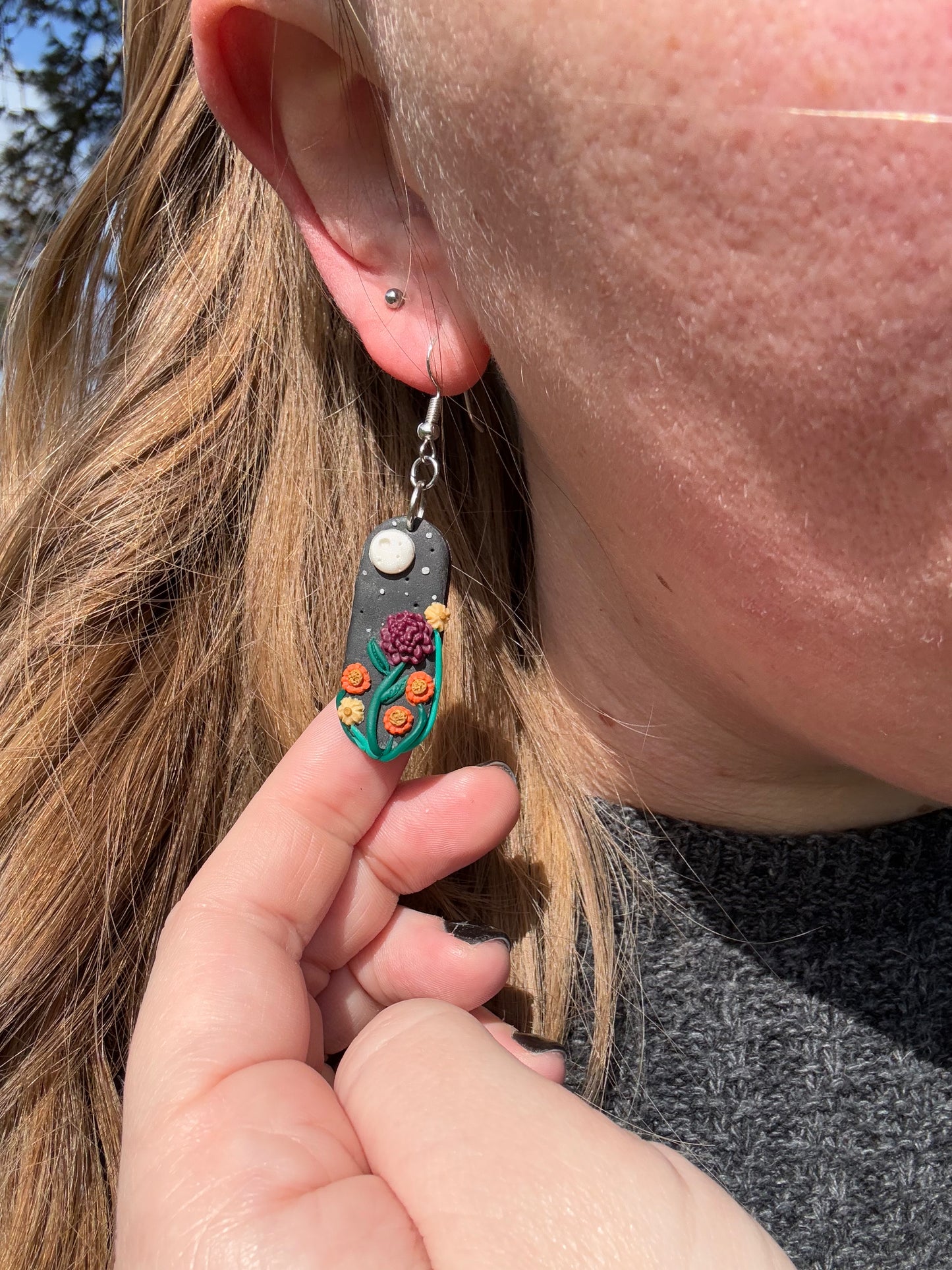 Capsule shaped black earring with a full moon ornament and a burgundy flower with 5 smaller yellow and orange smaller flowers.