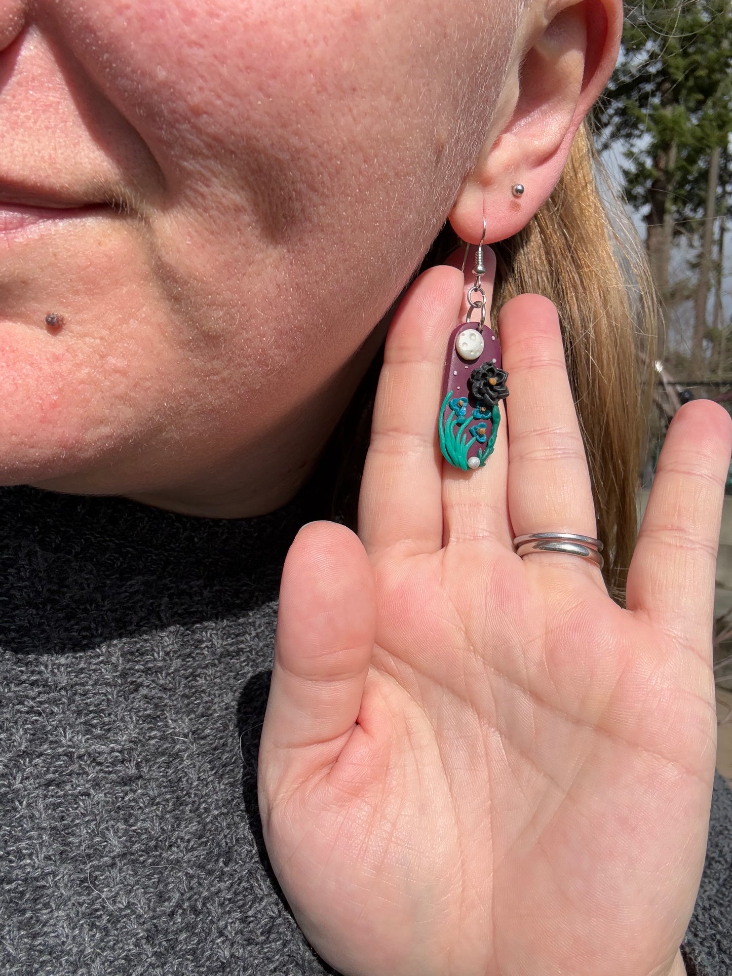 Capsule-shaped purple earring with a full moon ornament and a black rose with long grass.